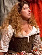 The Jailer's Daughter, in country patterned Elizabethan dress, kneels on the floor looking up in distraction with the legs of the Morris dancers behind her.